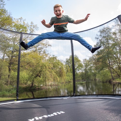 Lifestyle afbeelding van een kind dat springt op de VirtuFit Premium Trampoline met een stevig veiligheidsnet in een groene tuin.