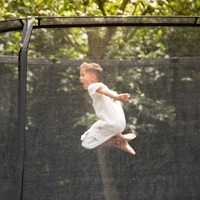 Sfeerbeeld van de VirtuFit Premium Trampoline waarbij de fijne mazen van het veiligheidsnet en de stabiele constructie tijdens het springen zichtbaar zijn.