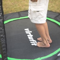 Detailopname van de zwarte springmat met het witte VirtuFit logo en de contrasterende groene randafwerking van de 140 cm kindertrampoline.