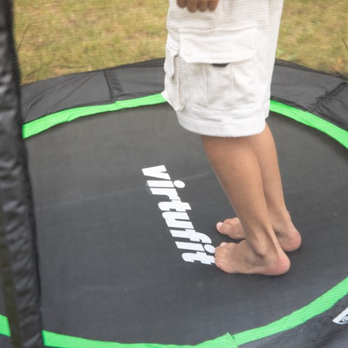 Detailopname van de zwarte springmat met het witte VirtuFit logo en de contrasterende groene randafwerking van de 140 cm kindertrampoline.